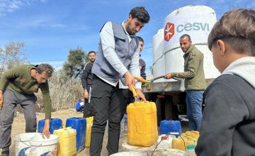 Several people filling yellow and white containers with water from a large white water tank labeled 'cesvi' in an outdoor setting under a clear blue sky